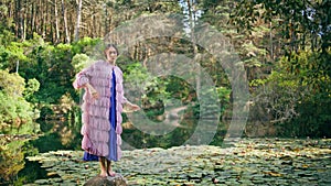 Beautiful forest nymph standing on stone at nature lake. Fantasy model posing