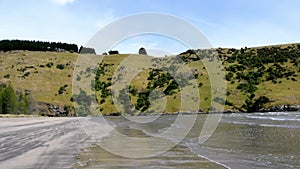 Beautiful forested hill and beach waves in Okains Bay, New Zealand