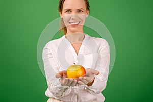 A beautiful forty-year-old woman holds a fresh apple in her hands on a green background. Healthy eating, vegetarianism, healthy