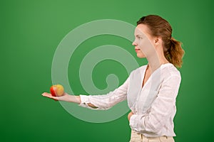 A beautiful forty-year-old woman holds a fresh apple in her hands on a green background. Healthy eating, vegetarianism, healthy