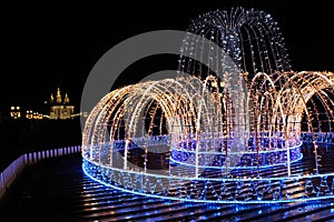 Beautiful fountain of colored holiday garlands glittering in city park in winter