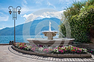 Beautiful fountain at lake shore Gardasee, tourist resort Limone with colorful impatiens flowers