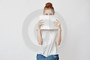 Beautiful foxy girl hiding face behind book looking at camera.