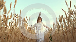 A beautiful, free, young farmer girl walks along a grain field and touches her hand with ripe spikelets of wheat. The