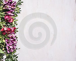 Beautiful freesya multicolored flowers with green leaves border ,place for text wooden rustic background top view