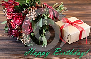 Beautiful fresh flower arrangement of red roses, gift box and text wish, birthday greeting card concept.