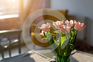 Beautiful fresh pink tulips bouquet in green glass vase on table in warm sunset sun lights against balcony window in