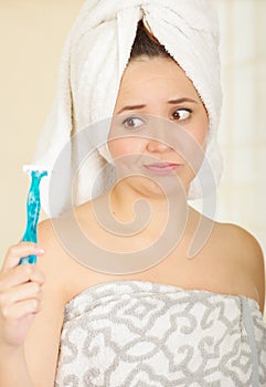 Beautiful fresh young unhappy girl with after shower towel holding blue razor