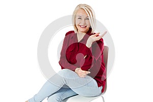 Beautiful friendly middle-aged woman sitting on a chair in isolation copy space