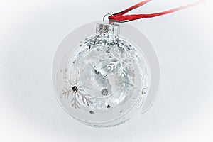 Beautiful frosty glittery clear Christmas ball ornament with snowflakes and a winter secone reflected inside it on soft snowy