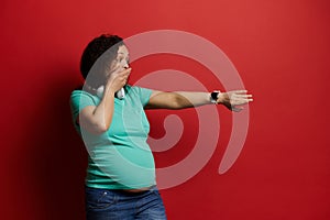 Beautiful frustrated pregnant woman checks contractions on mobile application on her wrist watch isolated red background