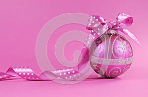 Beautiful fuchsia pink festive bauble ornament with polka dot ribbon on a feminine pink background with copy space