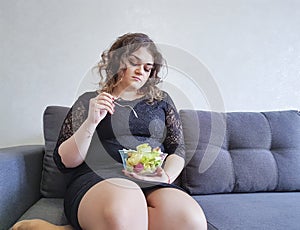 Beautiful full-length girl sitting lifestyle lettuce on the couch with a plate of salad
