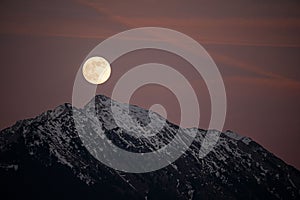 Beautiful full moon setting over majestic snow covered mountains.