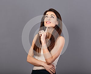 Beautiful fun grimacing wincing thinking business woman looking up with hand under the face in white formal t-shirt on grey
