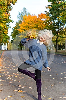 Beautiful fun happy blond girl jumping and having fun in autumn Park with a bouquet of bright colored leaves