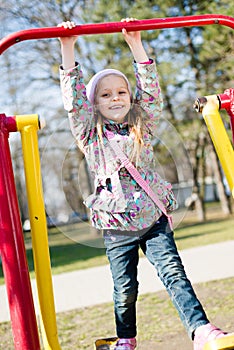 Beautiful funny cute little girl having fun riding a swing looking at camera & happy smiling in the park on spring or autumn