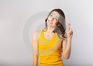 Beautiful funny humor smiling woman crossing the fingers making the wish to good luck and looking up in casual yellow t-shirt on
