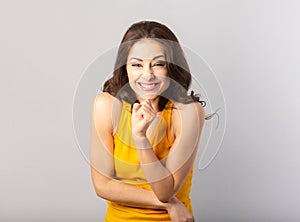 Beautiful funny humor smiling woman screwing up one`s eye making a wish  in casual yellow t-shirt on grey background with empty
