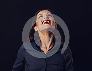 Beautiful funny toothy laughing business woman with wide open mouth looking up in blue shirt on black background with empty copy