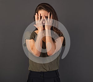 Beautiful funny young business peeping woman hiding from palms, covering the face the hands on grey background. Closeup. Emotion