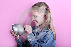 Beautiful funny young girl with silver piggy bank on pink background. save money concept.