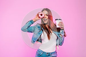 Beautiful funny young woman in stylish denim jacket with cup of tea or coffee posing with donut in the glaze near the glamorous