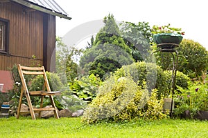 Beautiful garden with blooming flower beds and a wooden garden chair near country house