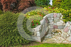 Beautiful garden with grass lawn and flowers in bloom and stone wall. Lush landscaped garden with colourful flowerbeds