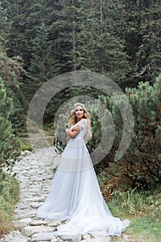 Beautiful gentle girl bride in the air fairy blue wedding dress with luxurious curls in the mountains near the lake with a crown u