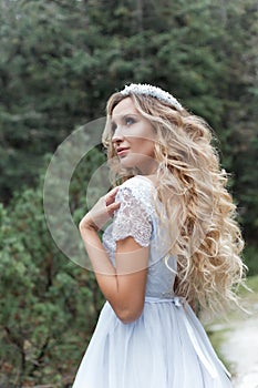 Beautiful gentle girl bride in the air fairy blue wedding dress with luxurious curls in the mountains near the lake with a crown u