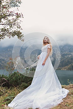 Beautiful gentle girl bride in the air fairy blue wedding dress with luxurious curls in the mountains near the lake with a crown u