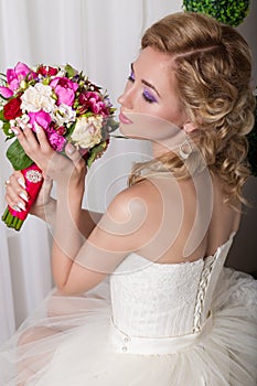 Beautiful gentle young girl happy bride in a white dress sitting on a chair and smelling a bridal bouquet with a nice manicure