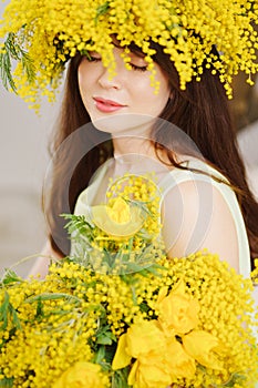 beautiful gentle young woman brunette with a bouquet and in a wreath of mimosa