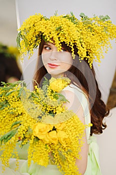beautiful gentle young woman brunette with a bouquet and in a wreath of mimosa