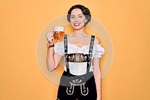 Beautiful german woman with blue eyes wearing traditional octoberfest dress drinking jar of beer with a happy face standing and