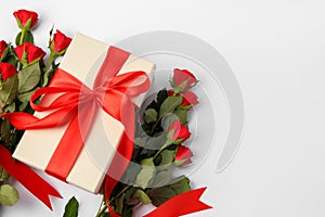 Beautiful gift box with bow and red roses on white background, flat lay. Space for text