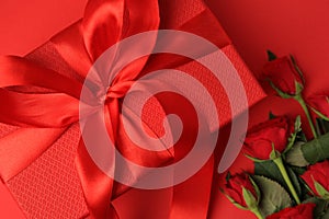 Beautiful gift box with bow and roses on red background, flat lay