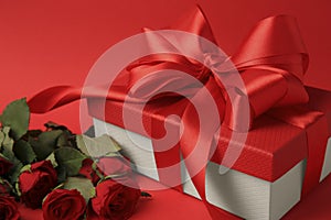 Beautiful gift box with bow and roses on red, closeup