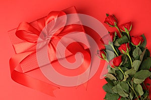 Beautiful gift box with bow and roses on red, flat lay