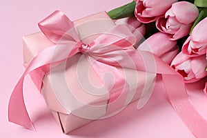 Beautiful gift box with bow and tulip flowers on pink background, closeup