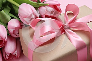 Beautiful gift box with bow and tulip flowers on pink background, closeup