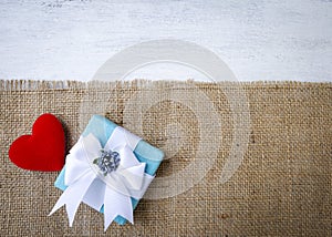 Beautiful gift box with red heart on hessian fabric with space on white wood texture background