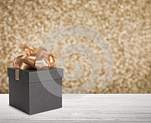 Beautiful gift box on white wooden table against shiny golden background, bokeh effect. Space for text