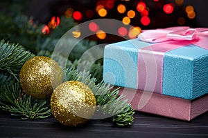 Beautiful gift wrapping in blue colors tied with a pink ribbon next to a Christmas tree decorated with toys