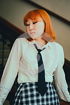 A beautiful ginger Asian schoolgirl in a white shirt and black tie stands poised in school, exuding both confidence and intellect