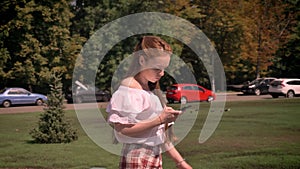 Beautiful ginger young woman typing on phone and walking on street, wearing shirt with bare shoulders, greeting somebody