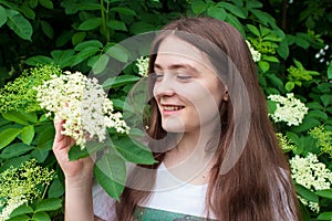 Beautiful girl 13 years old with long hair and an elder tree. Summer bloom in June, human unity with nature or natural