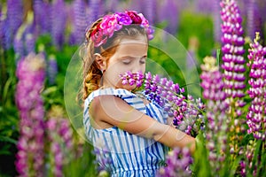 Beautiful girl 5 years old in the field with lupins. A meadow with purple flowers and a little girl with a wreath on her head. A