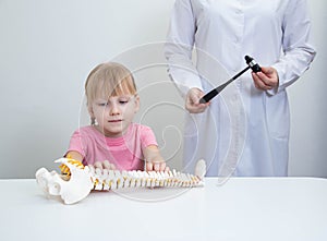 A beautiful girl 5 years old sits at the table and looks at the layout of the spine. A doctor in a white coat with a neurological